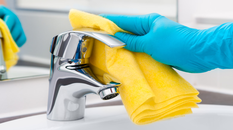 Hand wiping a bathroom sink faucet with a yellow cloth