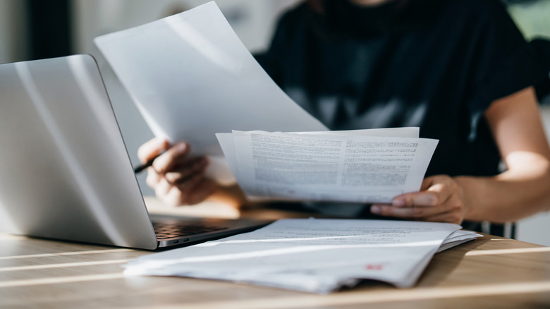 Woman holding documents near a laptop