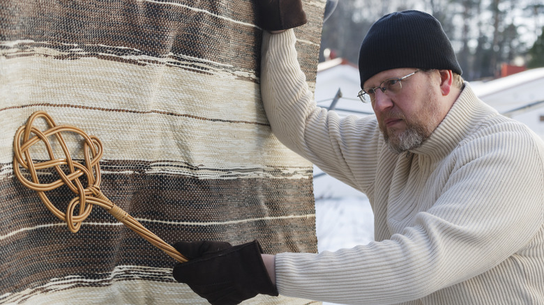 man using a carpet beater to clean his rug
