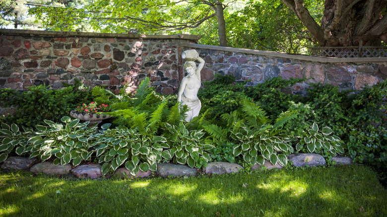 a shaded garden with a statue next to a brick wall