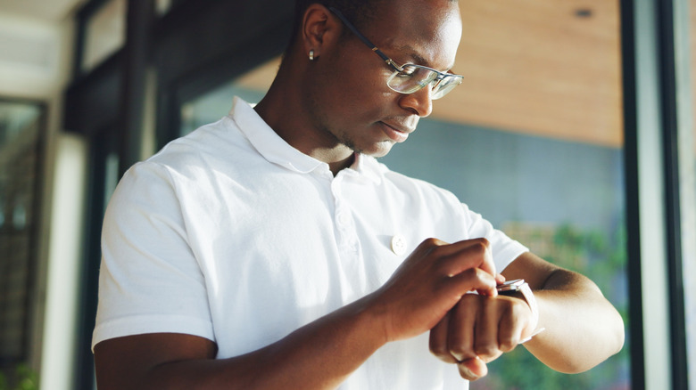 Man standing in front of glass doors and looking at his wristwatch