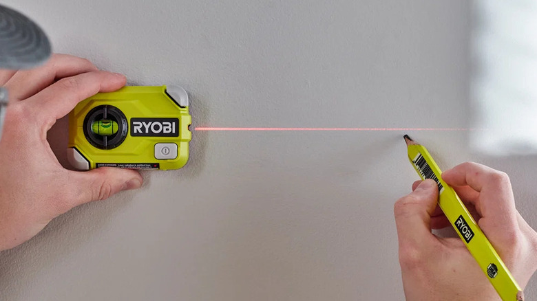 A person setting a level on a wall with Ryobi's 15-foot Compact Laser Level