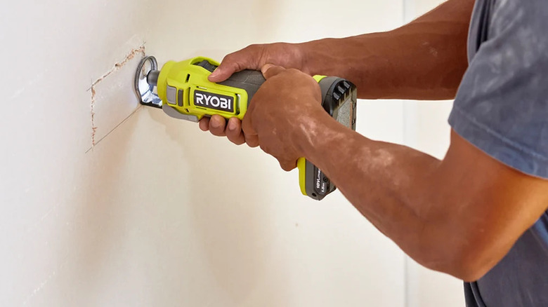 A person cutting out a hole for an electrical socket with Ryobi's 18V One+ Cordless Cut-Out Tool