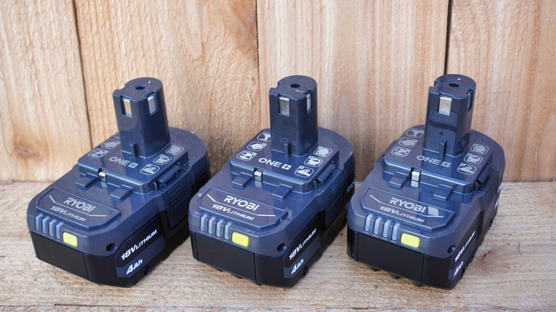 A line-up of Ryobi batteries against a wooden fence
