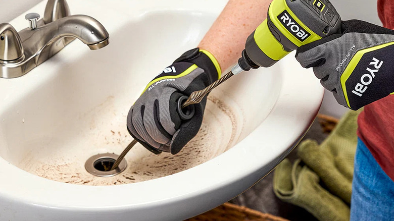 A person clearing a blocked sink with Ryobi's USB Lithium Cordless Drain Auger