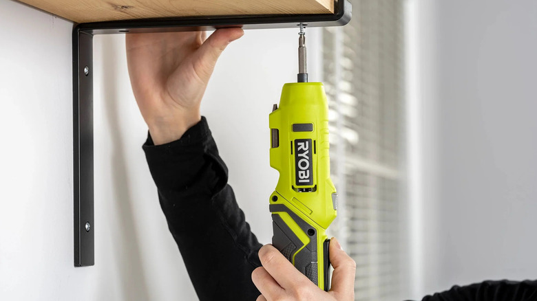 A person fixing screws into a shelf bracket with Ryobi's USB Lithium Screwdriver Kit