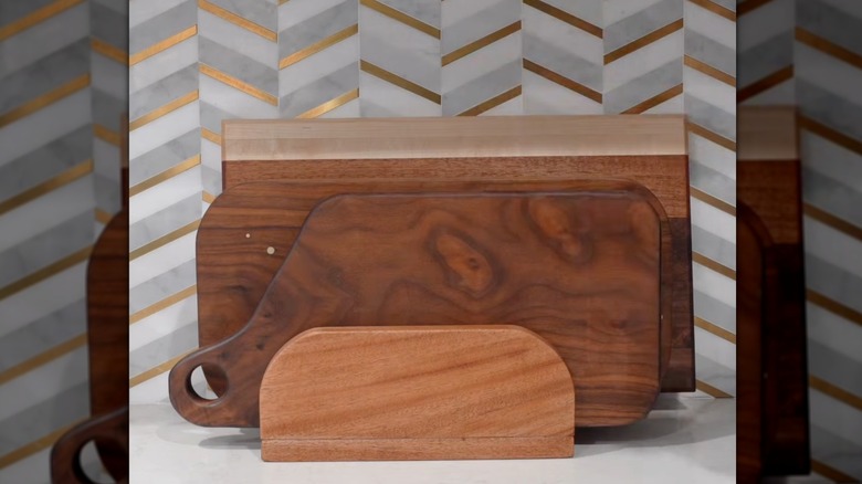 Three cutting boards resting in a wood holder on a counter in front of a chevron backsplash