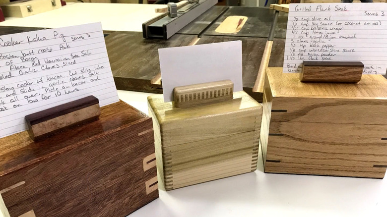 Three recipe boxes on a bench in a woodworking shop with recipe cards on top in card holder slots