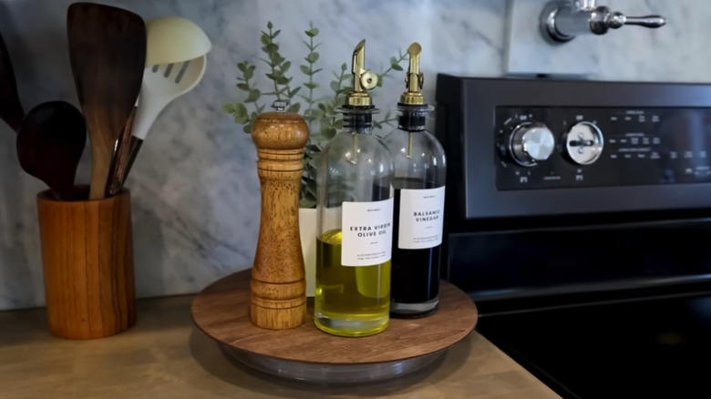 Oils in glass bottles, a pepper mill, and a plant on a circular shelf near a stove