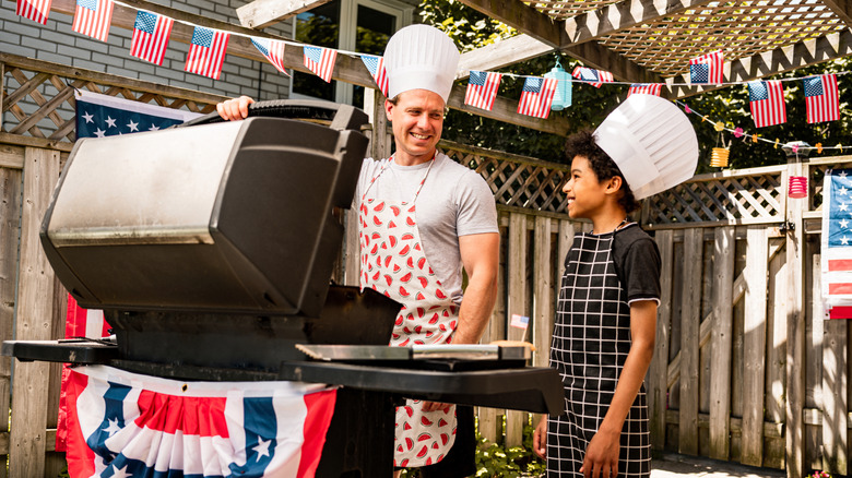 Father and son smiling and looking at a BBQ grill while celebrating the 4th of July