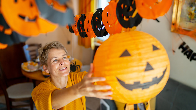 A smiling woman is hanging a jack-o-lantern in her home for Halloween