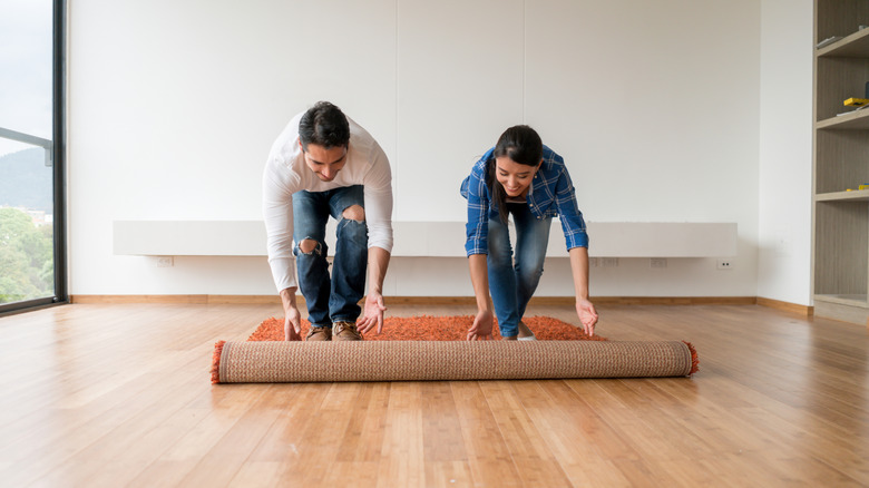 A smiling couple is unrolling a rug in their home
