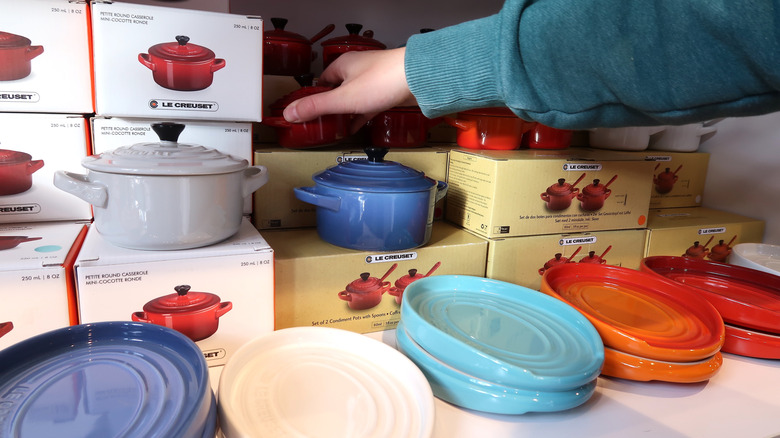 A sweater-covered arm reaching for a red Le Creuset Dutch oven in a store