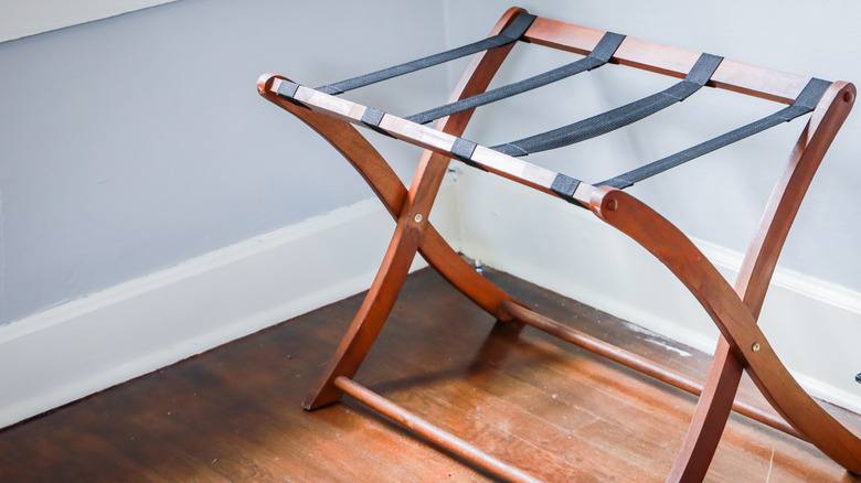 wooden luggage rack with black straps in the corner of room