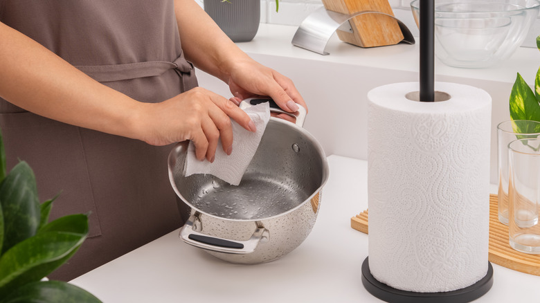 Hands drying a cooking pot with a paper towel