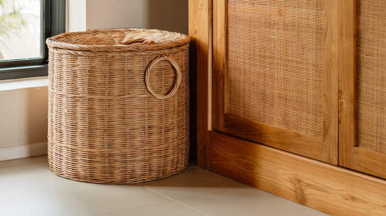 Wicker laundry basket next to wooden wardrobe with rattan doors