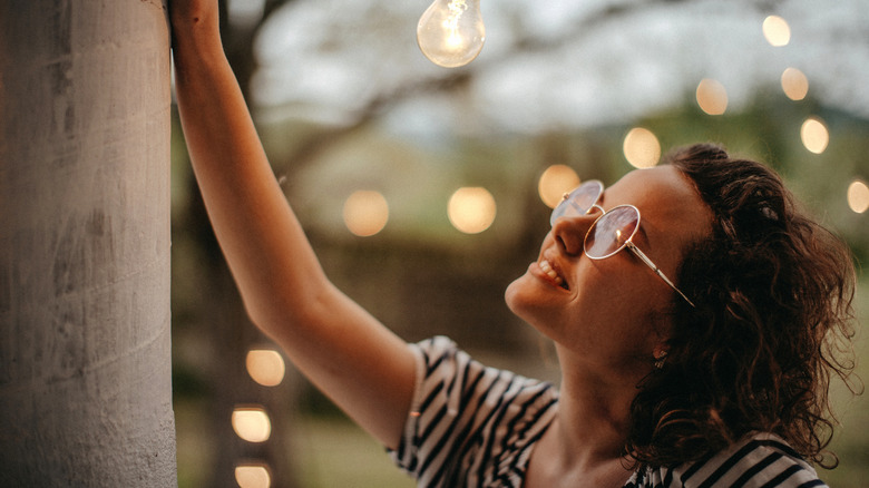 A person smiling by a tree strung with outdoor lights
