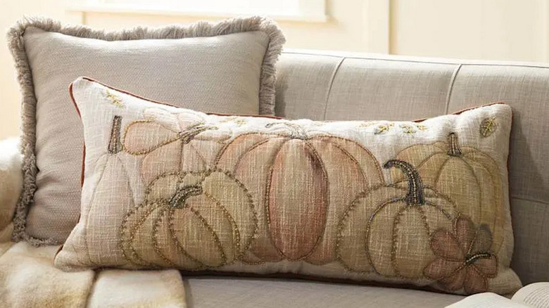 A long throw pillow with neutral colors, with pumpkins and stitched into it