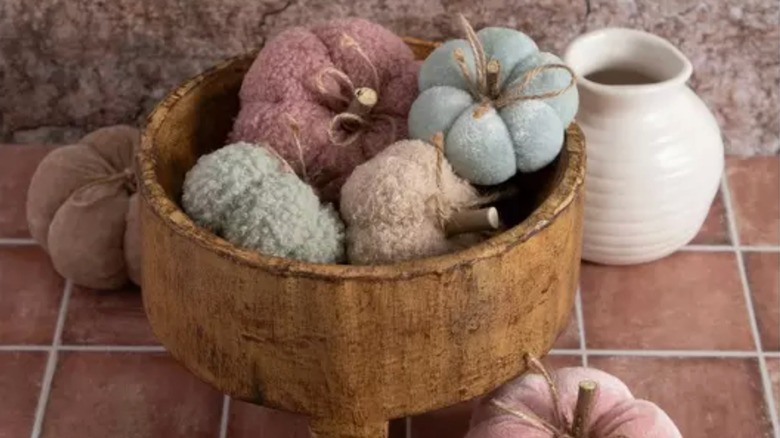 A wooden bowl on a tiled counter filled with pimpkins made of twine and different fabric textures and colors