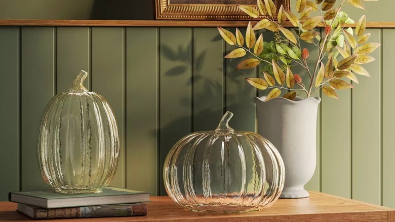 Two glass pumpkins on an entranceway table with a sage-green background