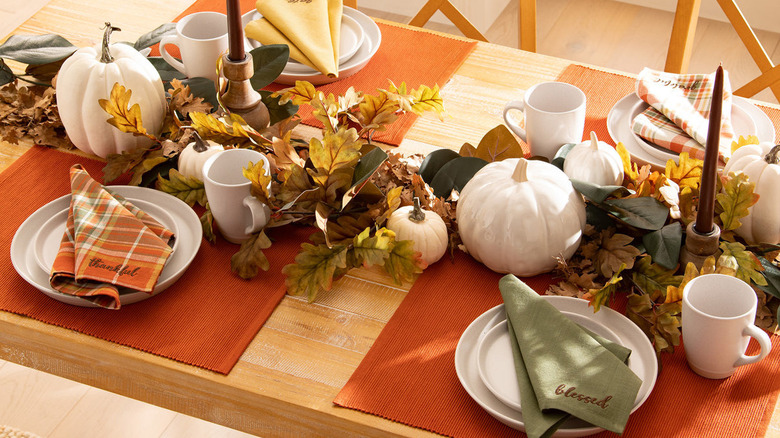 A table set up with Thanksgiving decor, including orange placemats, pumpkins, candles, and napkins