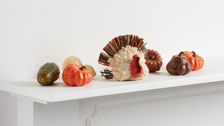 A white background with several gourds and a natural fiber turkey on a white mantel