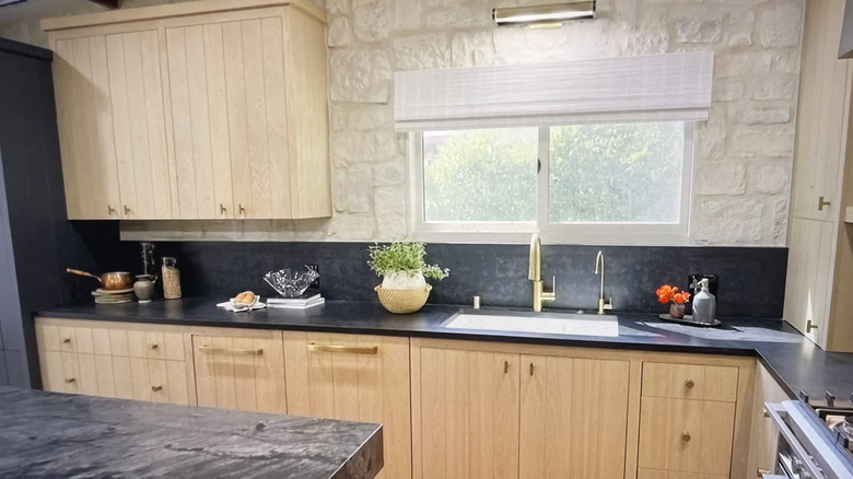 Rustic kitchen with neutral wood cabinetry and black marble backsplash paired with brass fixtures