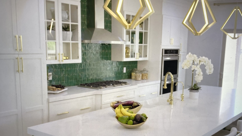 Modern kitchen with white cabinetry and counters around jewel-tone green tile backsplash.