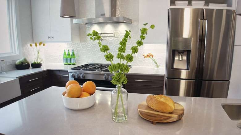 Bright kitchen with white island counter, stainless appliances, and hexagonal white backsplash