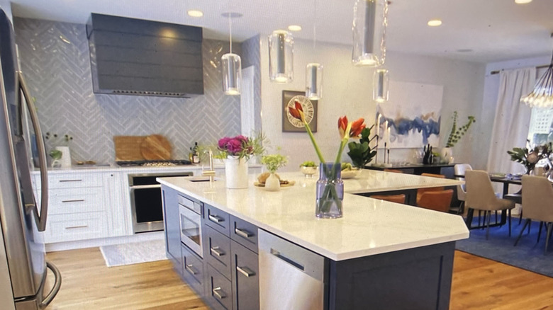 Open layout kitchen and dining area with L-shaped island, range, and hood in front of herringbone subway tile