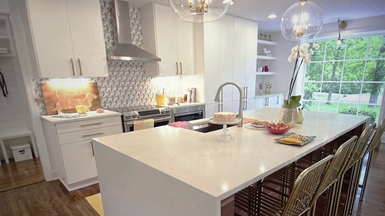 Bright kitchen with white island and cabinetry and stainless range and hood paired with geometric gray tile