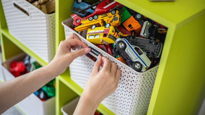 Someone stashing away toy trucks in a white storage box