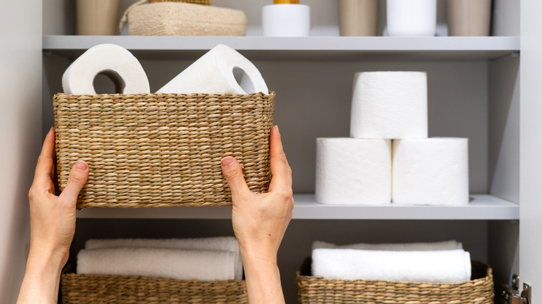 A person pulling out a wicker basket with toilet paper in it