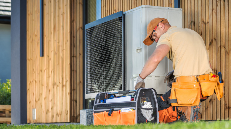 A contractor maintaining a modern heat pump outside of a house