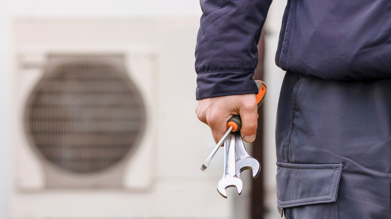 Close-up of a man holding tools with a blurred heat pump in the background