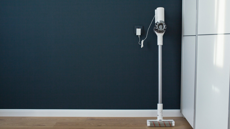 A cordless vacuum cleaner charging near a wall outlet on navy blue wall