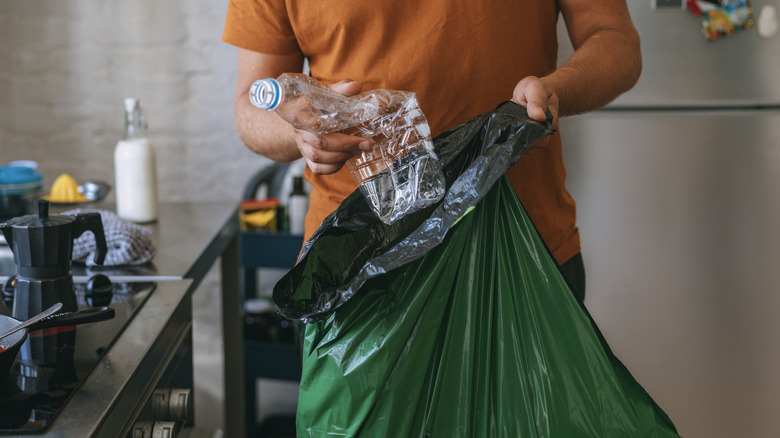 Young man filling trash bag in the kitchen in the evening with plastic water bottle