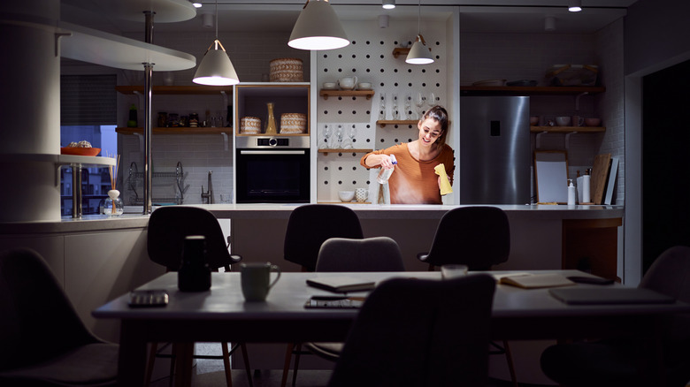 A young woman spraying and cleaning her kitchen counter at night