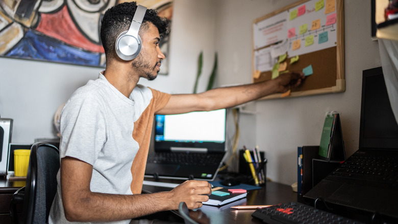 Young man organizing home workspace and sticking post-it to bulletin board