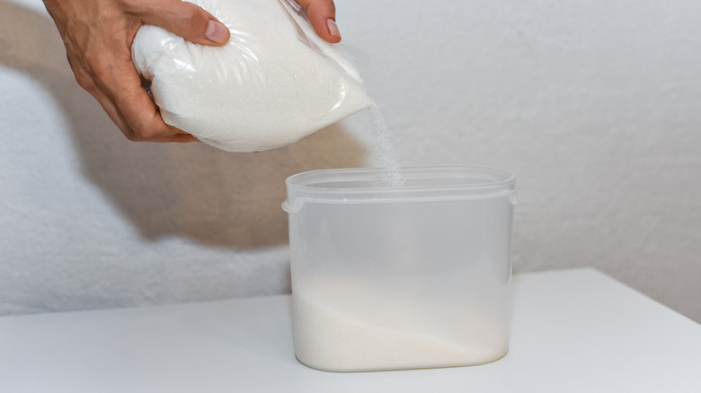 Hand pouring sugar inside plastic tupperware container