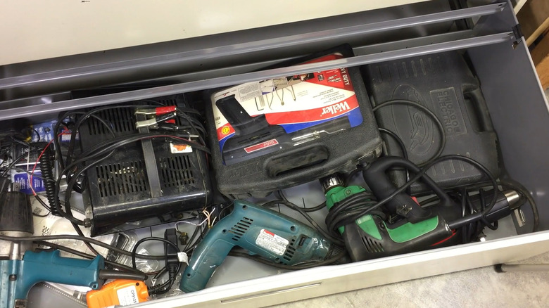 An open drawer in a lateral file cabinet filled with assorted tools in a garage