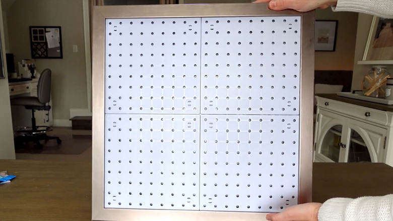 Woman holding up a small section of pegboard surrounded by a frame