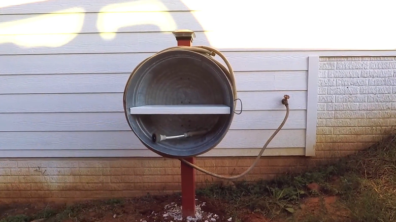 Large galvanized tub attached to a post with a hose wrapped around the bucket and a shelf inside
