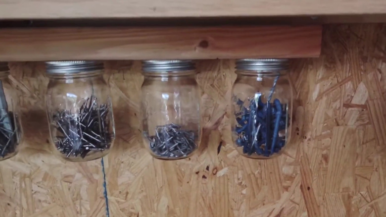 Row of jars hanging rom a piece of wood holding screws and other fasteners
