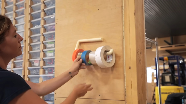 Person adjusting rolls of tape on a towel bar hanging on a garage wall