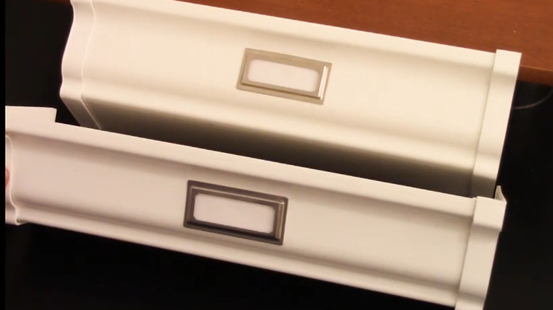 Two shelves made from sections of gutters with metal labels on the front