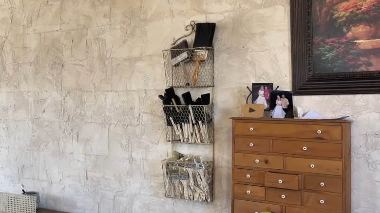Textured walls in garage with a metal rack installed holding various types of paint brushes