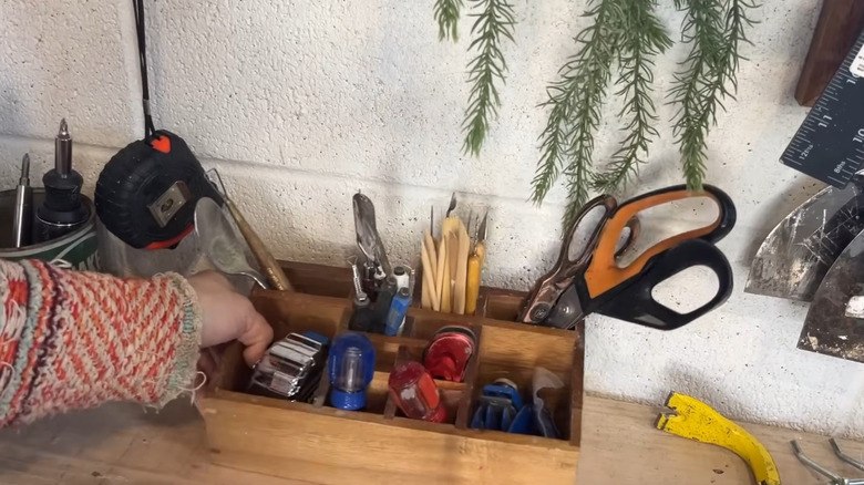 Woman positions a wooden divided box on the workbench of her garage to hold tape measures and small tools