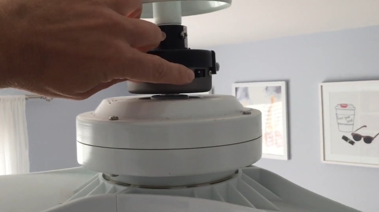 Finger flipping the switch on a white ceiling fan