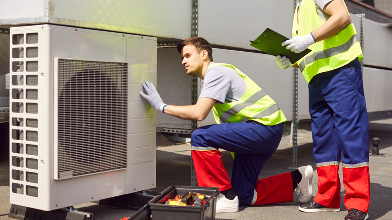 Two workers examining a HVAC system on the roof of a home